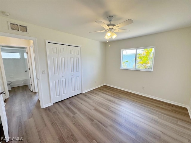 unfurnished bedroom featuring baseboards, visible vents, a ceiling fan, wood finished floors, and a closet