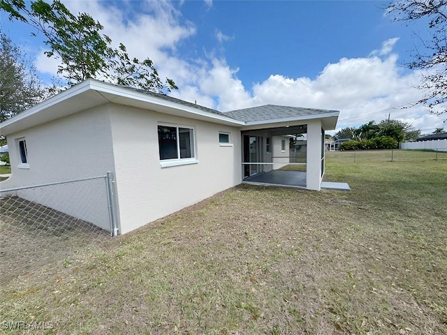 rear view of property with roof with shingles, a yard, stucco siding, a sunroom, and fence