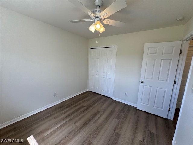 unfurnished bedroom with dark wood-type flooring, a closet, baseboards, and a ceiling fan