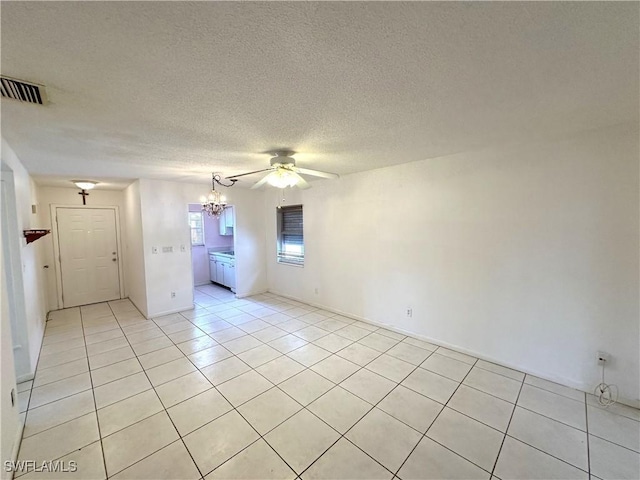 unfurnished room with light tile patterned floors, a textured ceiling, ceiling fan with notable chandelier, and visible vents