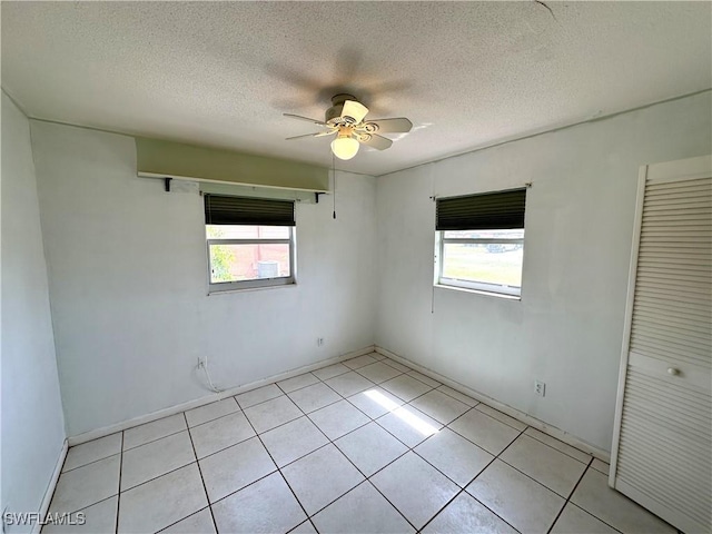 empty room featuring light tile patterned floors, ceiling fan, a textured ceiling, and a wealth of natural light