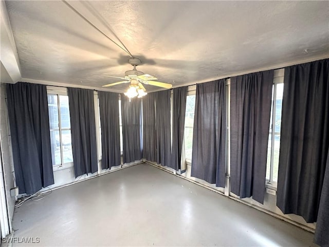 spare room featuring a healthy amount of sunlight, a ceiling fan, and concrete flooring