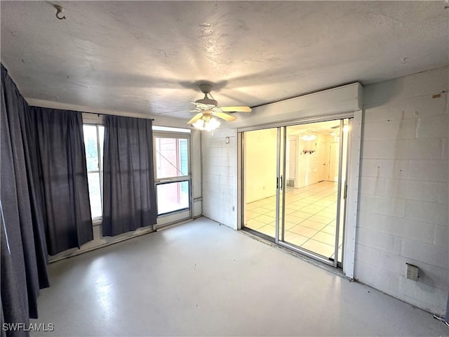 unfurnished room with concrete block wall, concrete floors, and a ceiling fan