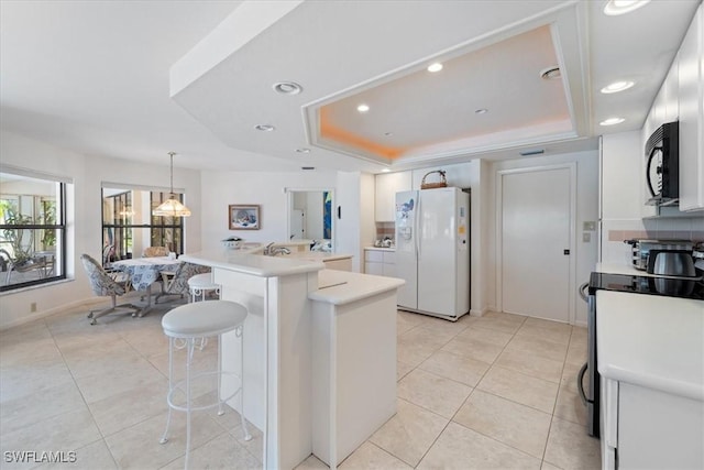 kitchen featuring a tray ceiling, white cabinets, white fridge with ice dispenser, black microwave, and stainless steel electric range