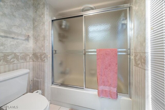 bathroom with combined bath / shower with glass door, tile walls, toilet, and tile patterned floors