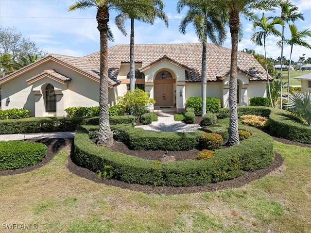 mediterranean / spanish-style home with a tile roof, a front yard, and stucco siding