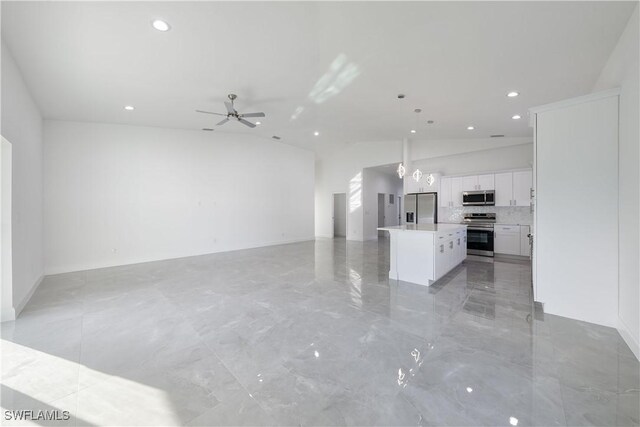 kitchen with a kitchen island, open floor plan, stainless steel appliances, light countertops, and white cabinetry