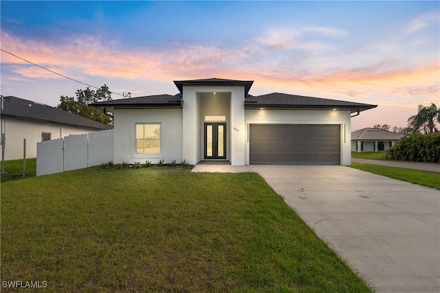 prairie-style home with an attached garage, fence, driveway, a lawn, and stucco siding