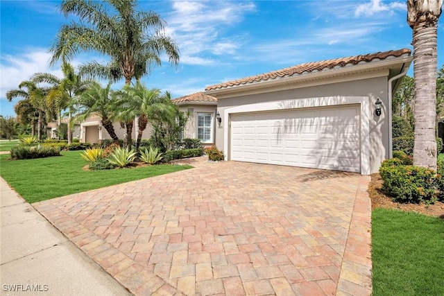 mediterranean / spanish-style house featuring a garage, stucco siding, a tile roof, decorative driveway, and a front yard