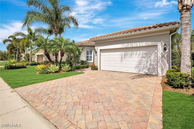 mediterranean / spanish-style house with decorative driveway, stucco siding, a garage, a front lawn, and a tiled roof