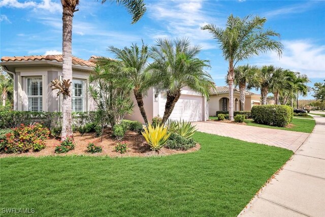 mediterranean / spanish house with driveway, a garage, a front yard, stucco siding, and a tiled roof