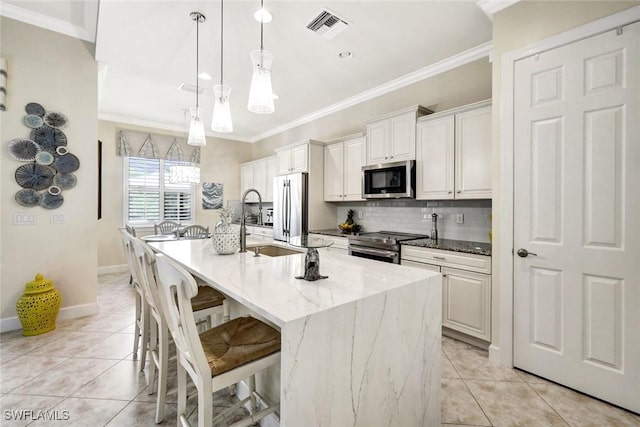 kitchen with stainless steel appliances, light tile patterned floors, a kitchen island with sink, ornamental molding, and tasteful backsplash