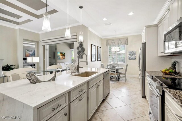 kitchen with a sink, appliances with stainless steel finishes, a kitchen island with sink, hanging light fixtures, and light stone countertops