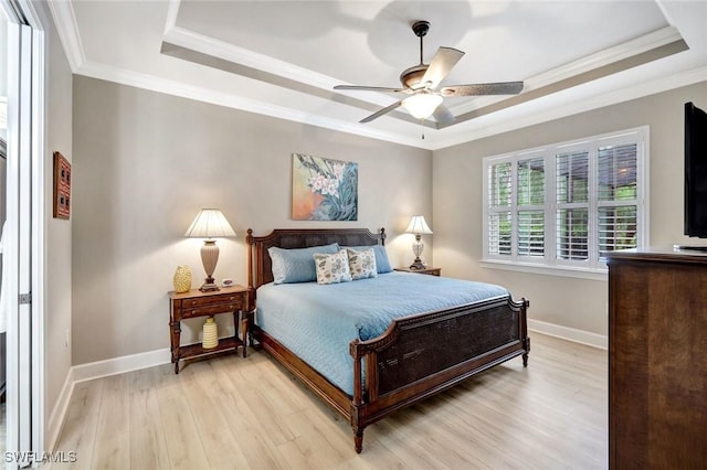 bedroom featuring light wood-type flooring, baseboards, a tray ceiling, and crown molding