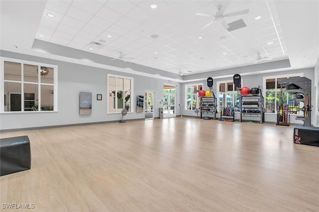 exercise room with a tray ceiling, wood finished floors, a ceiling fan, and baseboards