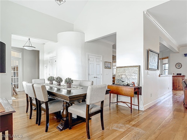 dining area featuring light wood finished floors, baseboards, high vaulted ceiling, and crown molding