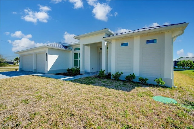 prairie-style house featuring an attached garage, a front yard, a standing seam roof, metal roof, and driveway