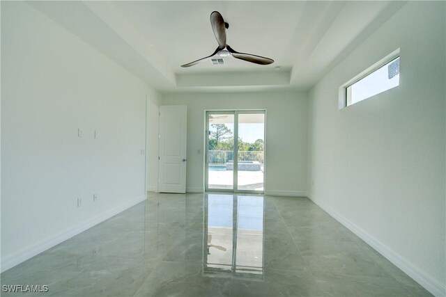 empty room with baseboards, visible vents, a tray ceiling, and ceiling fan