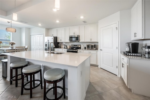 kitchen featuring visible vents, a kitchen bar, a kitchen island with sink, a sink, and appliances with stainless steel finishes