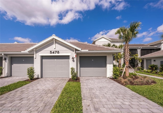 ranch-style house featuring stucco siding, a tiled roof, decorative driveway, and a garage