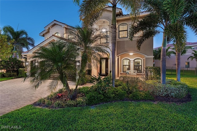 mediterranean / spanish home with stucco siding, a front lawn, decorative driveway, fence, and a balcony