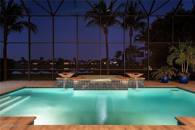 pool at night with glass enclosure, an in ground hot tub, an outdoor pool, and a patio