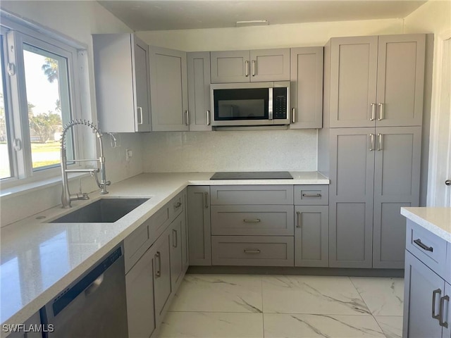 kitchen with decorative backsplash, marble finish floor, stainless steel appliances, gray cabinetry, and a sink