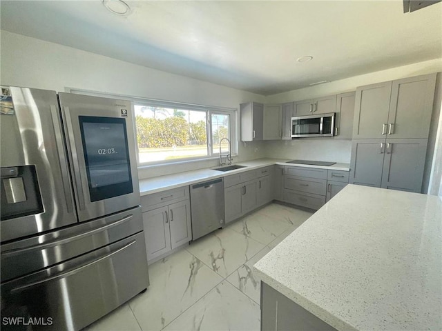 kitchen featuring marble finish floor, stainless steel appliances, a sink, and gray cabinetry