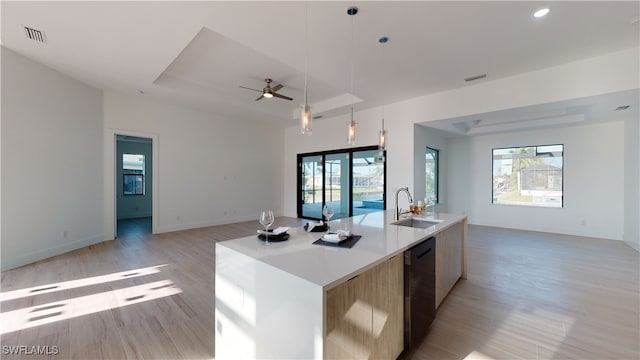 kitchen featuring a tray ceiling, hanging light fixtures, light wood-style flooring, open floor plan, and a sink