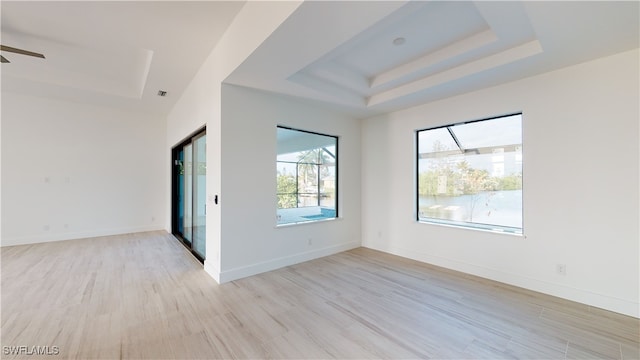 empty room with light wood-style floors, visible vents, baseboards, and a raised ceiling