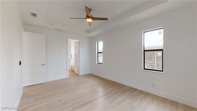 unfurnished bedroom with baseboards, a raised ceiling, and light wood-style floors