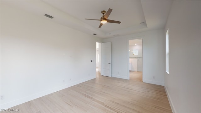 unfurnished bedroom with light wood-style floors, a tray ceiling, visible vents, and baseboards