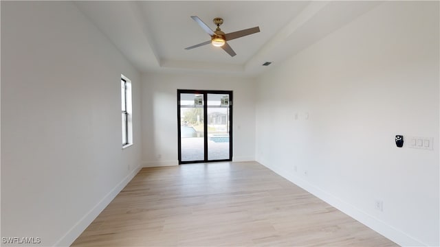 unfurnished room featuring ceiling fan, visible vents, light wood-style floors, baseboards, and a tray ceiling