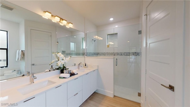 full bathroom featuring double vanity, visible vents, wood finished floors, a shower stall, and a sink