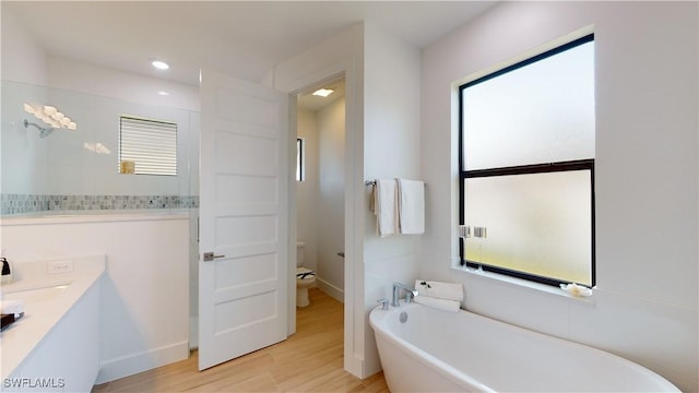 bathroom with recessed lighting, a soaking tub, toilet, vanity, and wood finished floors