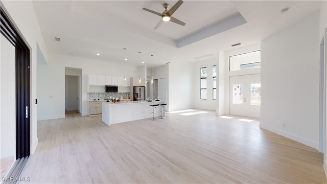 kitchen featuring white cabinets, open floor plan, a tray ceiling, stainless steel appliances, and backsplash