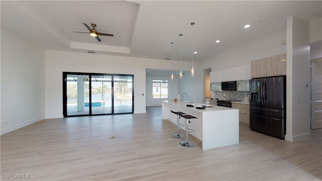 kitchen featuring a center island with sink, light countertops, open floor plan, modern cabinets, and black appliances