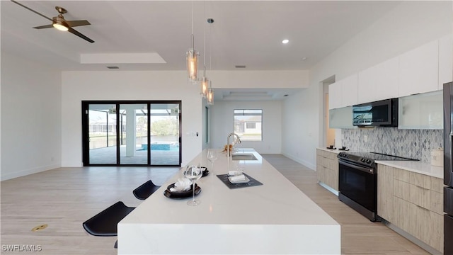 kitchen featuring black range with electric stovetop, a sink, open floor plan, stainless steel microwave, and modern cabinets