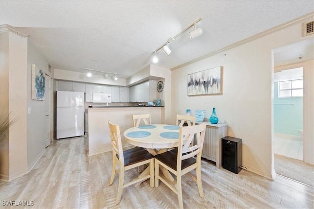 dining space with visible vents, light wood-style flooring, ornamental molding, a textured ceiling, and baseboards