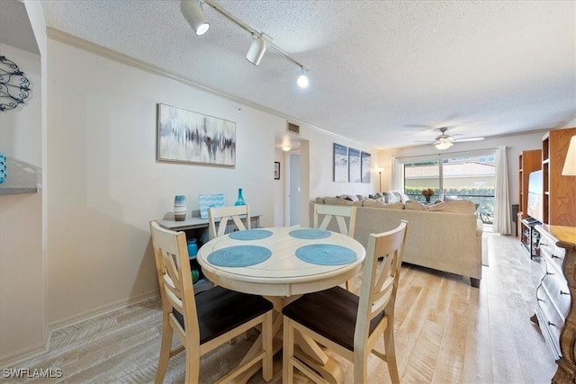 dining area featuring visible vents, light wood-style flooring, ornamental molding, a textured ceiling, and ceiling fan