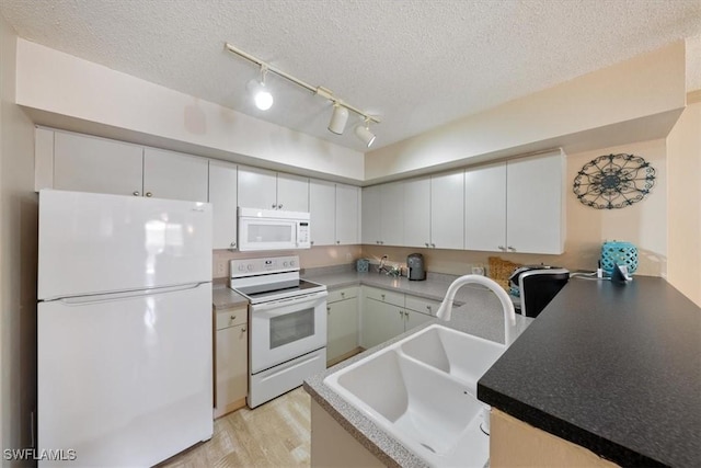 kitchen with white appliances, a peninsula, a sink, a textured ceiling, and light wood-type flooring