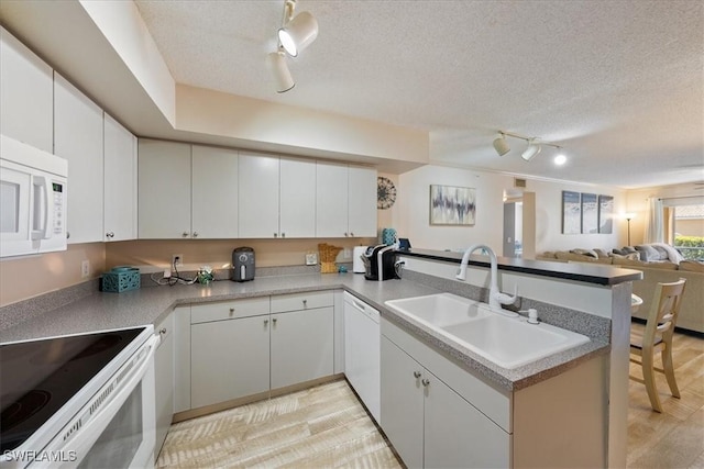 kitchen featuring a textured ceiling, white appliances, a peninsula, and a sink