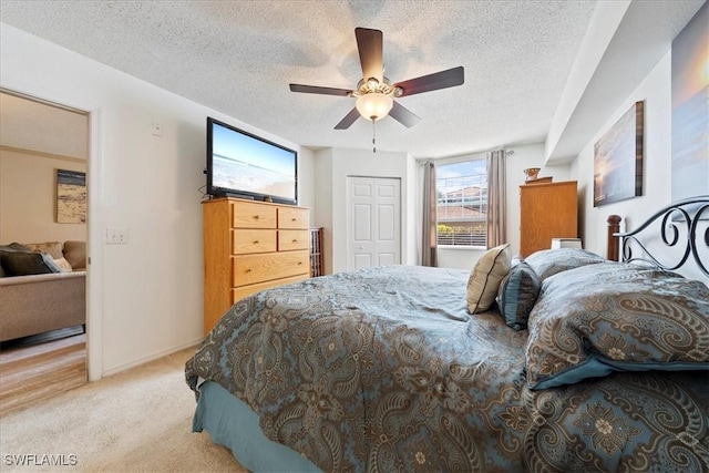 bedroom featuring a closet, light carpet, a textured ceiling, and ceiling fan