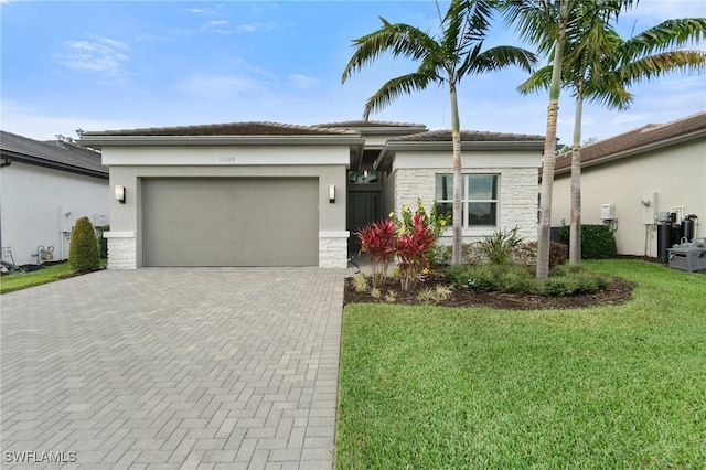 view of front of house featuring decorative driveway, a tile roof, stucco siding, an attached garage, and a front yard