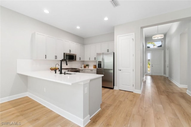 kitchen with visible vents, a peninsula, stainless steel appliances, light countertops, and a sink