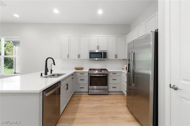 kitchen with stainless steel appliances, light countertops, light wood-style floors, a sink, and a peninsula