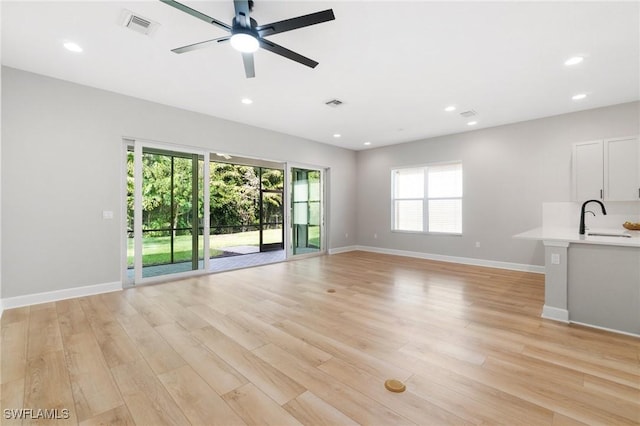 unfurnished living room with recessed lighting, visible vents, a sink, light wood-type flooring, and baseboards