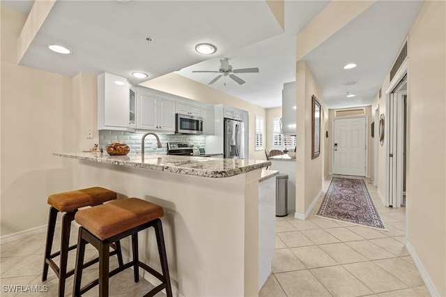 kitchen featuring a breakfast bar area, light stone countertops, a peninsula, appliances with stainless steel finishes, and tasteful backsplash