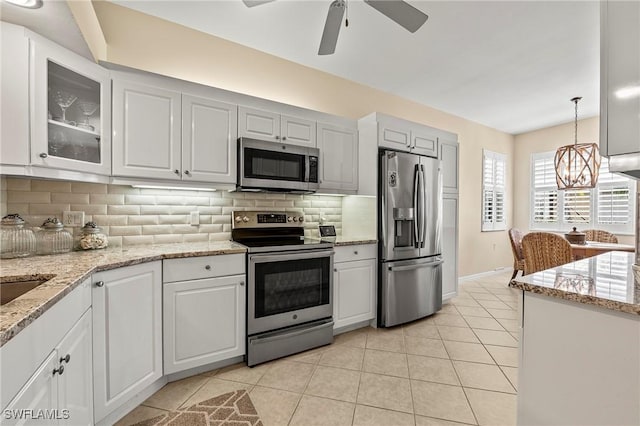 kitchen featuring backsplash, glass insert cabinets, light tile patterned floors, appliances with stainless steel finishes, and white cabinets