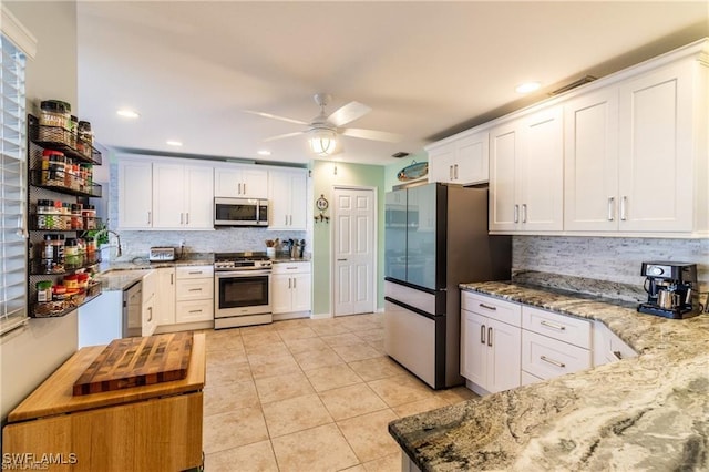 kitchen featuring light tile patterned floors, a ceiling fan, white cabinets, appliances with stainless steel finishes, and light stone countertops